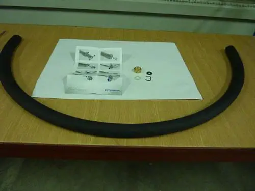 Flexibles Edelstahlrohr mit Zubehörteilen auf einem Tisch, einschließlich Dichtungen und Montageanleitung von Remeha.